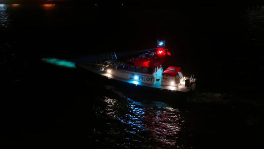 Boat with bright red, white, and blue navigation bulbs shining at night on water surface reflection