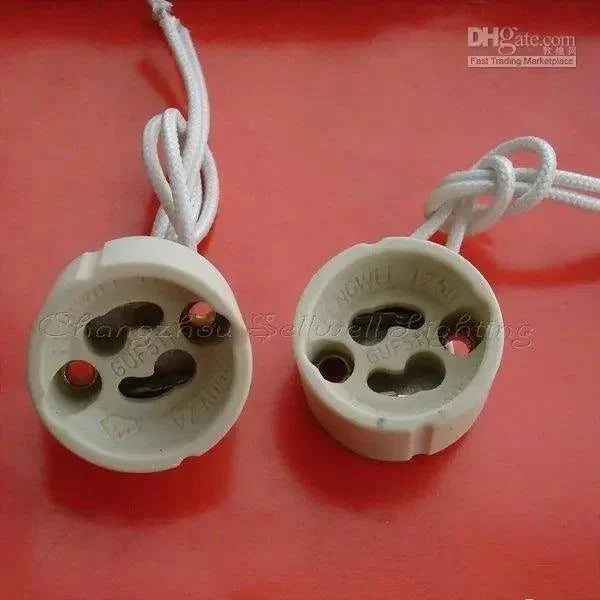 Close-up of two white GU10 ceramics lamp bases with attached wires on red background